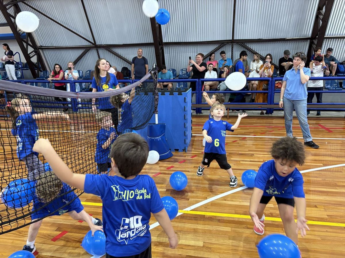Crianças do H10 Kids jogando com bexigas sobre a rede, com as famílias assistindo