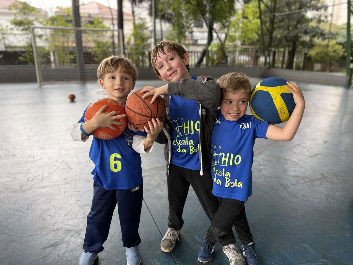 Três crianças do H10 Kids abraçadas, cada uma segurando a bola de um esporte diferente