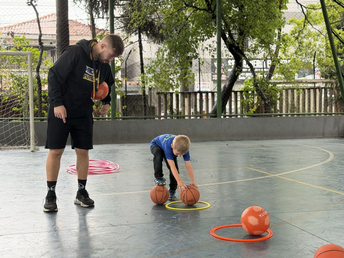 Professor do H10 Kids ensinando um menino a quicar a bola dentro de um arco